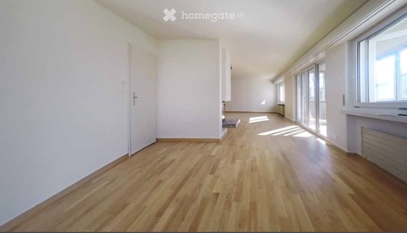 Empty room with wooden flooring, white walls, large windows, and a door leading to another area.