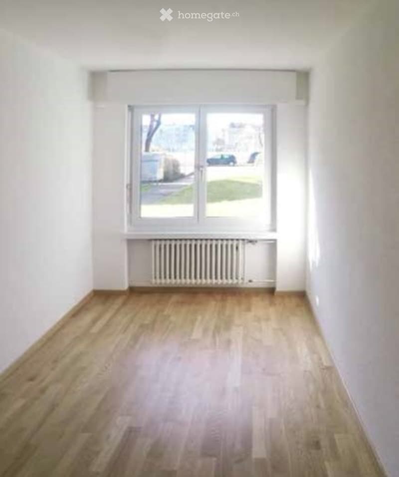 Empty room with wooden flooring, white walls, and a large window with a radiator below. No furniture or equipment present.