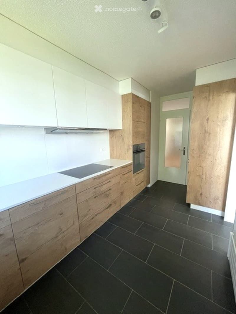 Modern kitchen with white and wooden cabinets, black tiled floor, and built-in appliances including an oven and stove.