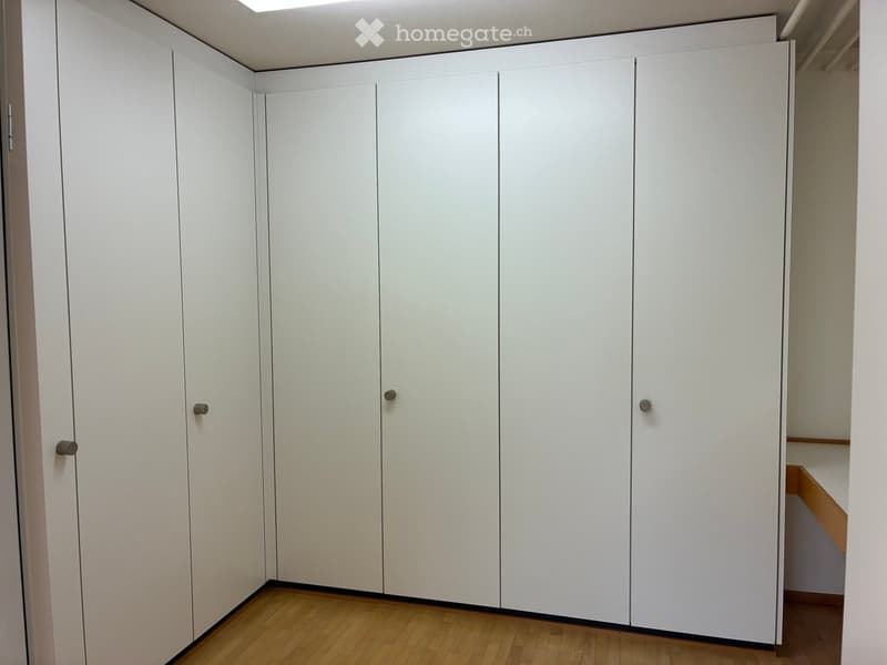 Empty room with white built-in wardrobes and wooden flooring.