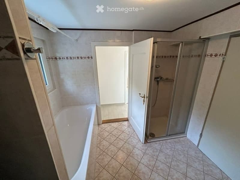 Bathroom with a bathtub, a glass-enclosed shower stall, and a door leading to another room.