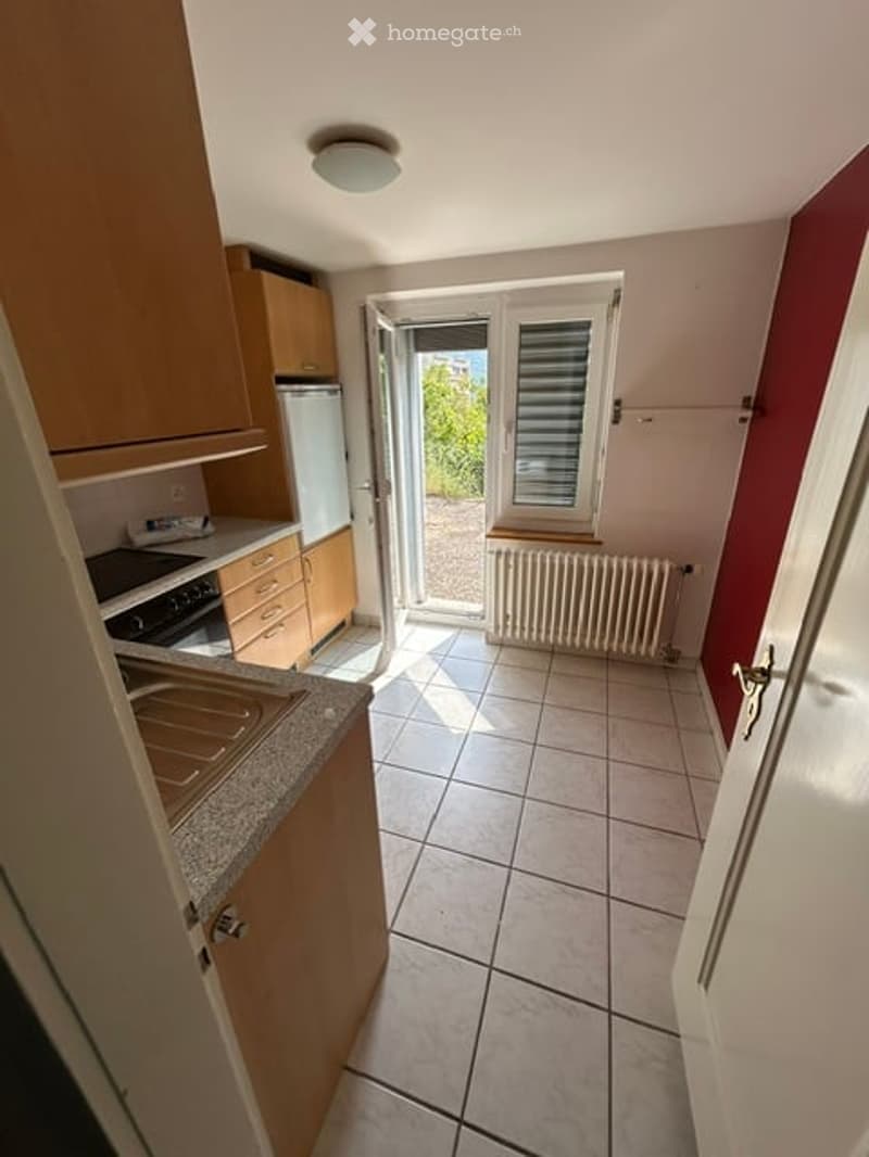 Modern kitchen with wooden cabinets, granite countertop, stainless steel appliances, and a view through an open door to a balcony area.