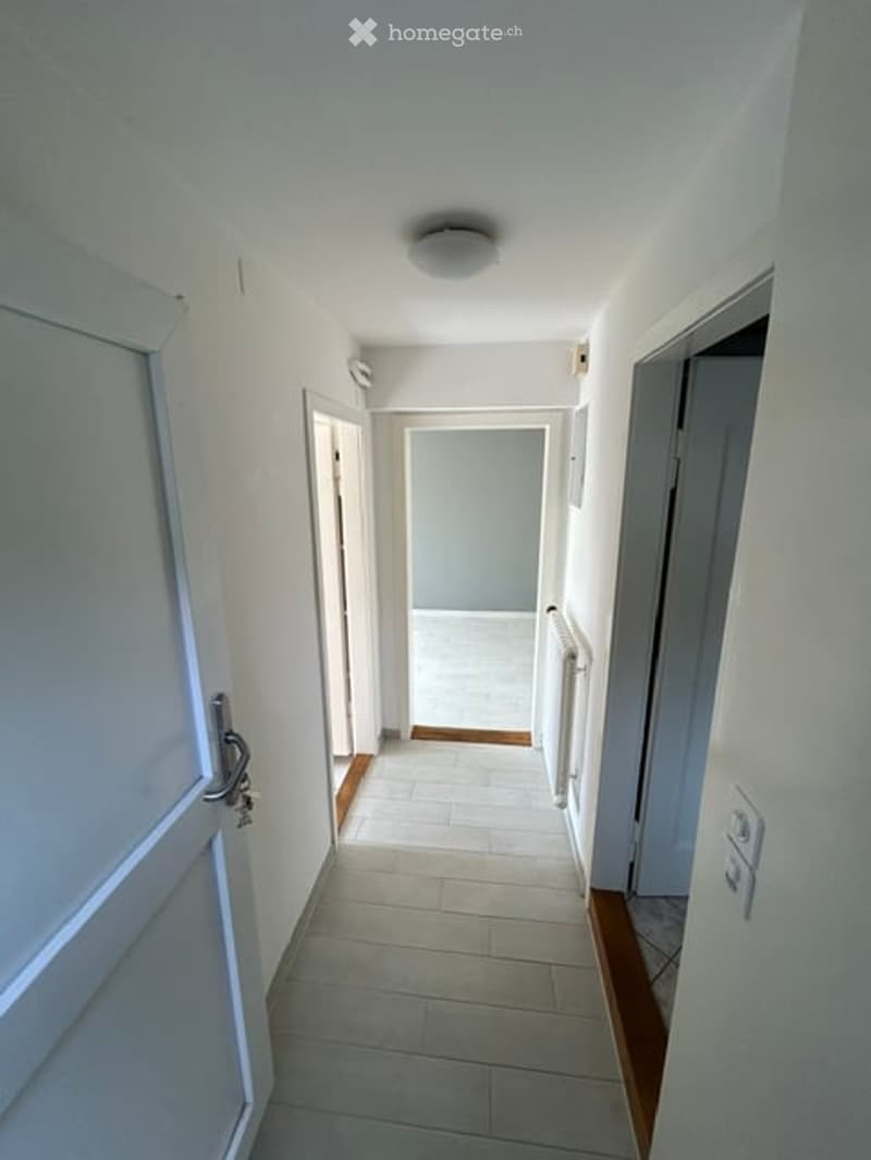 A clean, well-lit hallway with white walls, tiled flooring, and several doors leading to different rooms.