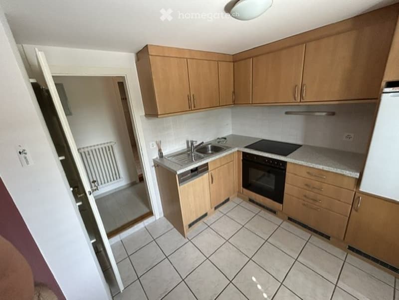 Modern kitchen with light wooden cabinets, tiled floor, and stainless steel appliances including a sink, dishwasher, and oven.