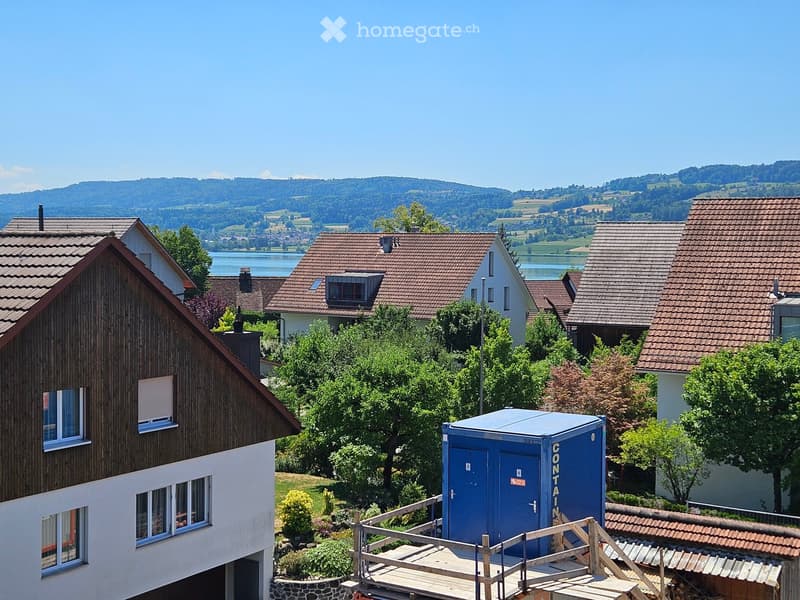 Residential houses with red-tiled roofs, surrounded by greenery and a scenic lake view in the background.