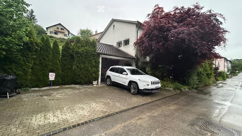 Two-story house with a garage, white SUV parked inside, surrounded by greenery and trees.