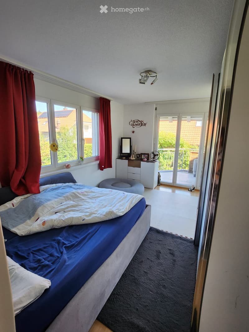 Well-lit bedroom with a large bed, nightstand, mirror, and a view of the balcony through large windows.