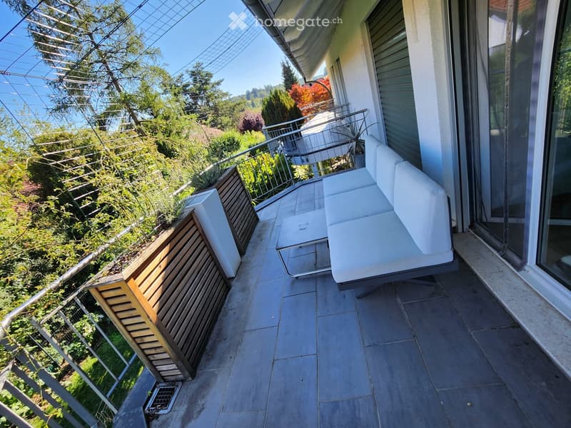 Balcony with a white sofa, small table, and wooden planters, overlooking a green garden.