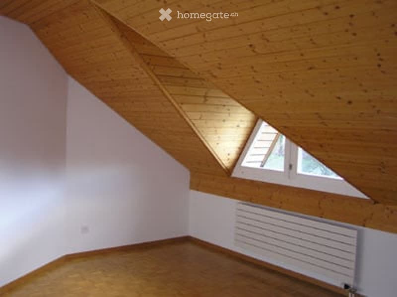 Empty attic room with wooden ceiling, exposed beams, skylight window, and wooden floor.