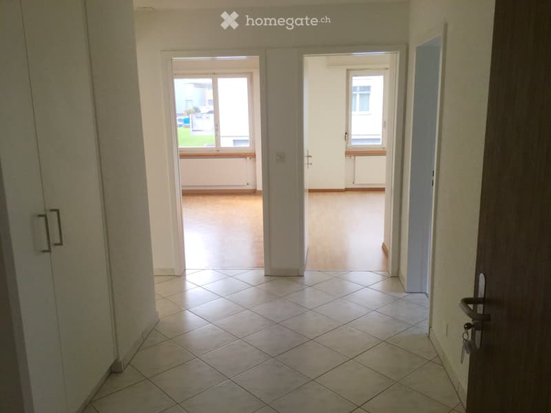 Empty hallway with tiled floor, white walls, and doors leading to two rooms with windows.