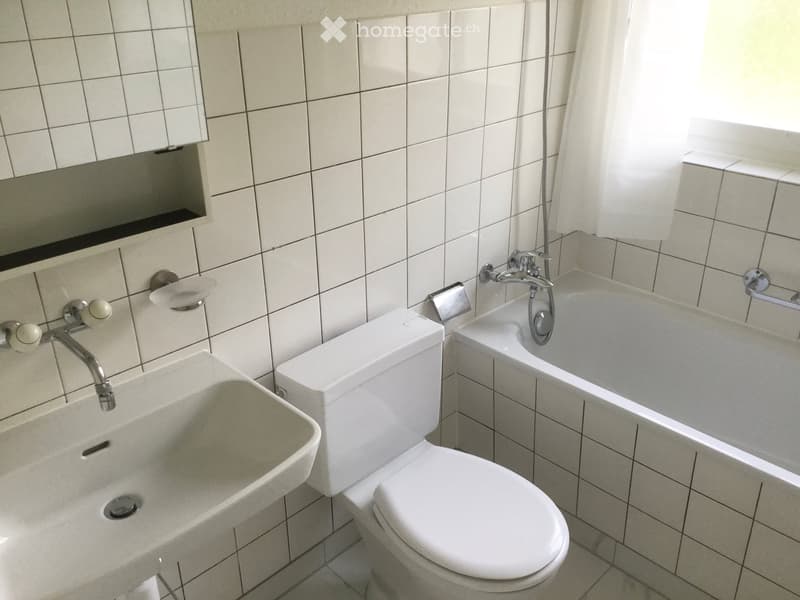 Modern bathroom with white tiles, a toilet, a sink, a bathtub, and a showerhead.
