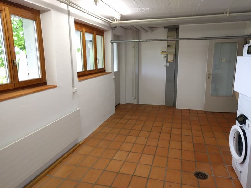 Empty room with tiled floor, white walls, wooden windows, and a washing machine in the corner.