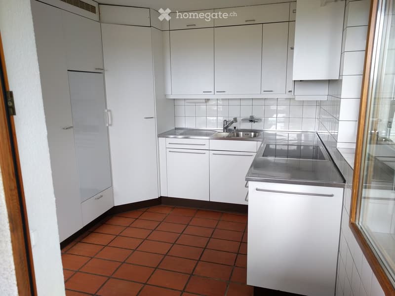 Modern kitchen with white cabinets, stainless steel sink, and red tiled floor.