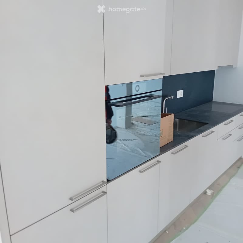 modern kitchen with white cabinets, black countertop, stainless steel sink, glass oven, faucet