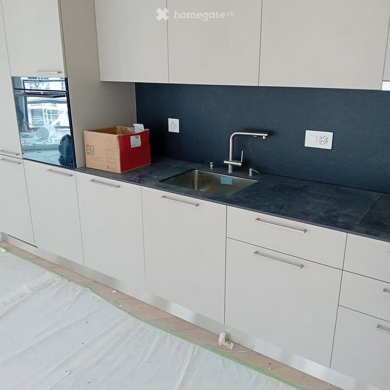 modern kitchen, white cabinets, gray countertop, stainless steel sink, faucet, electrical outlets, cardboard box, white floor