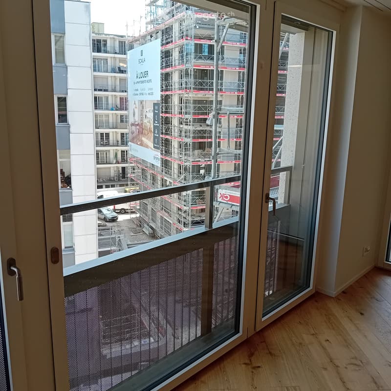 Empty room with wooden flooring and large glass balcony door leading to a view of a construction site.