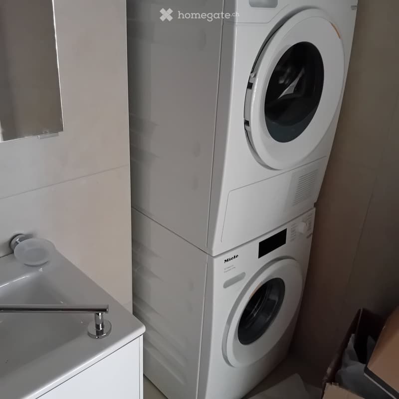A bathroom with a sink, a mirror, and a stacked washing machine and dryer.
