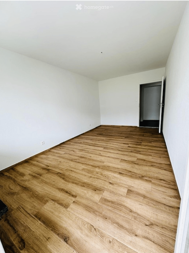 Empty room with wooden flooring and white walls, featuring a doorway leading to another room.