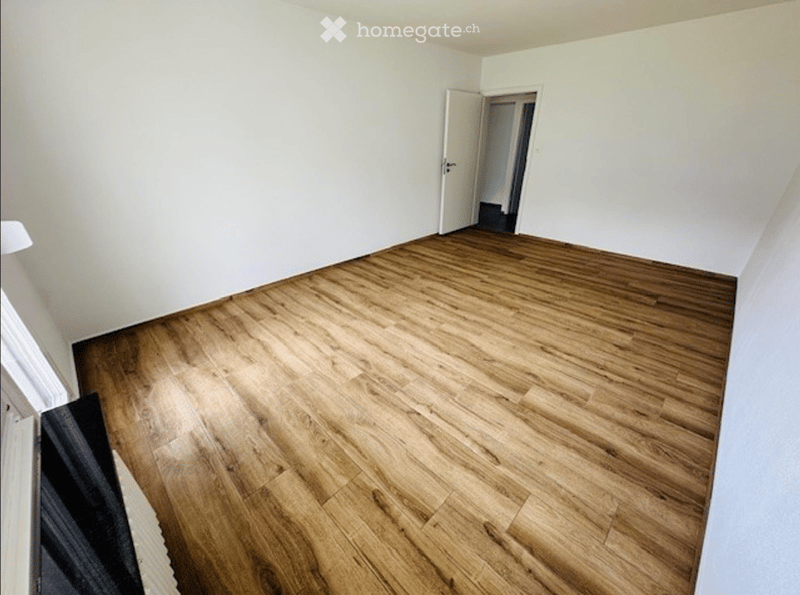 Empty room with wooden flooring and white walls, featuring an open doorway leading to another space.