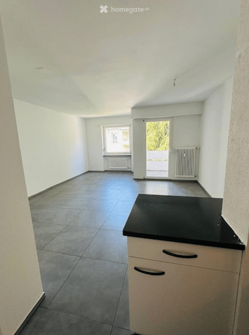 Empty room with tiled floor, white walls, and a small kitchen counter with cabinets. No furniture or personal items present.