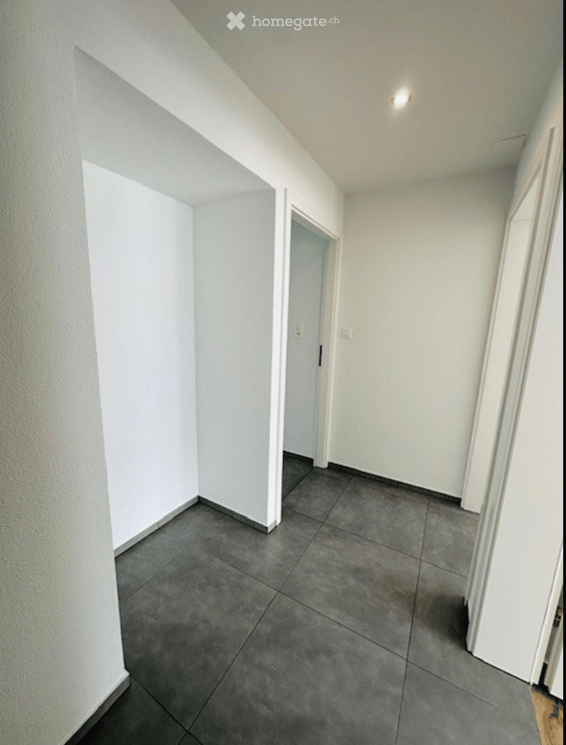 Empty hallway with grey tiled floor, white walls, and a single door leading to another room.