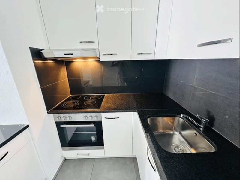 Modern kitchen with white cabinets, black countertops, stainless steel sink, induction cooktop, and built-in oven.