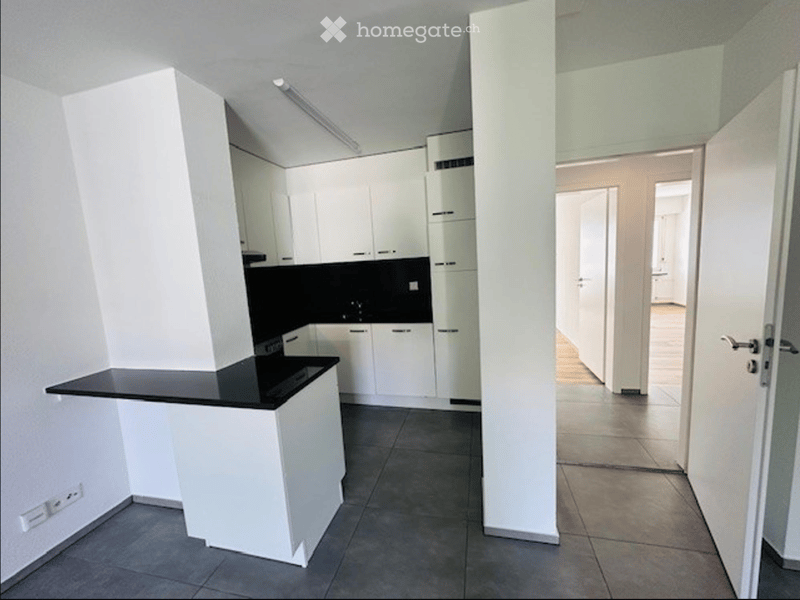 Empty kitchen area with white cabinets, black countertops, and tiled flooring. The space is clean and unfurnished, with no visible appliances or furniture.