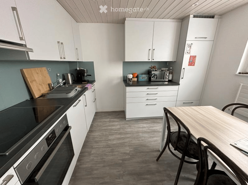 Modern kitchen with white cabinets, stainless steel appliances, and a wooden dining table with chairs.
