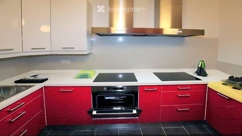 Modern kitchen with red lower cabinets, white upper cabinets, induction cooktop, oven, and stainless steel sink.