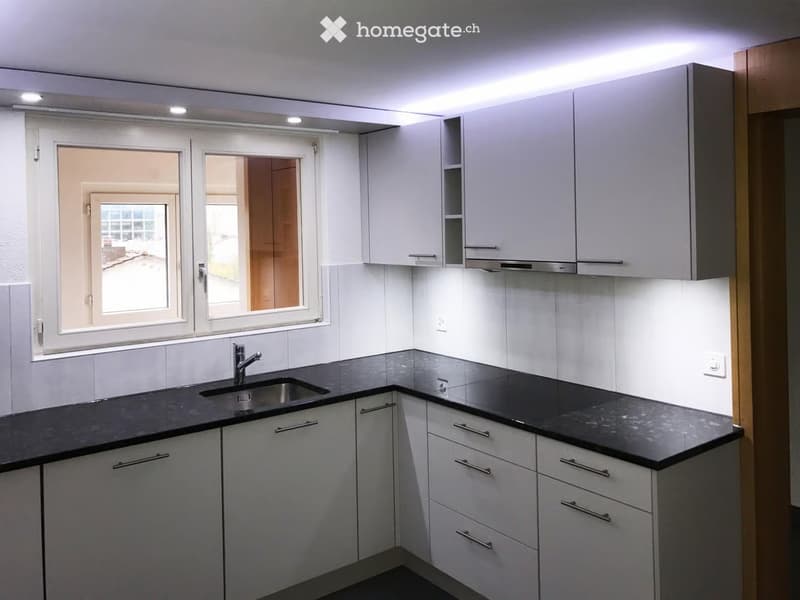 Modern kitchen with white cabinets, black countertops, and a stainless steel sink.