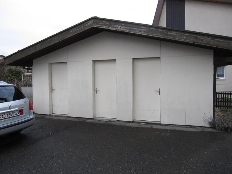 A modern, white garage with multiple doors and a sloped roof, situated on a paved driveway with a car parked nearby.