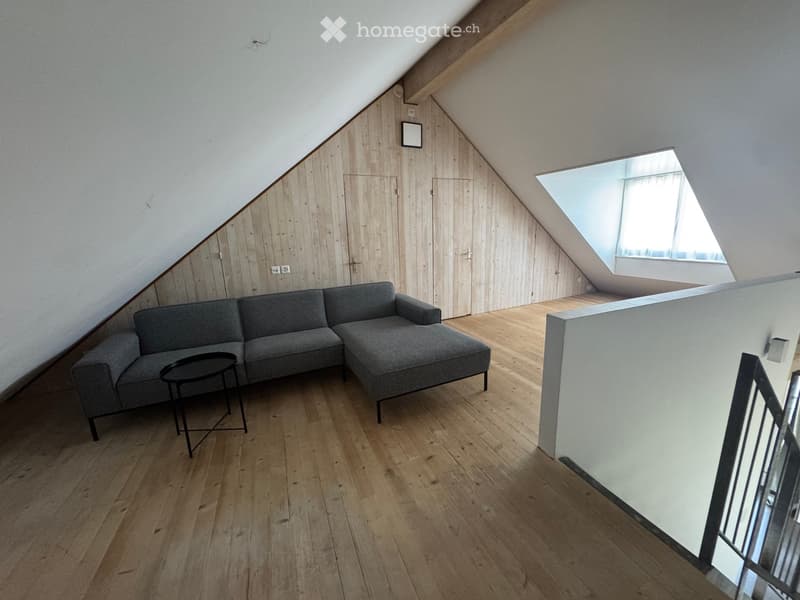 Modern living room with wooden floors, grey sectional sofa, black coffee table, and skylight window.