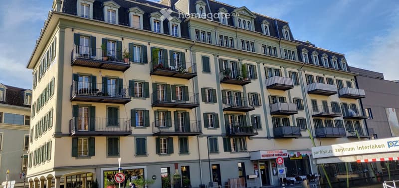 Multi-story building with multiple balconies, green shutters, and a restaurant on the ground floor.