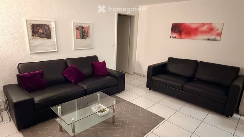 Modern living room with two black sofas, a glass coffee table, and two picture frames on the walls.
