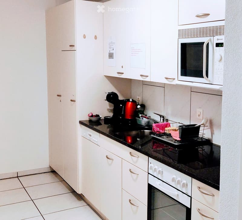 Modern kitchen with white cabinets, black countertops, microwave, oven, coffee maker, and dish rack.