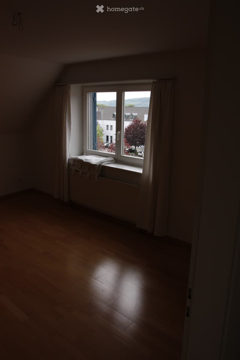 Empty room with wooden flooring and a window with blinds, showing a view of the outside.