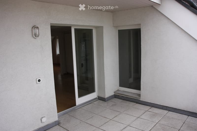 Balcony with tiled floor, sliding glass door leading to interior, and a wall-mounted light fixture.