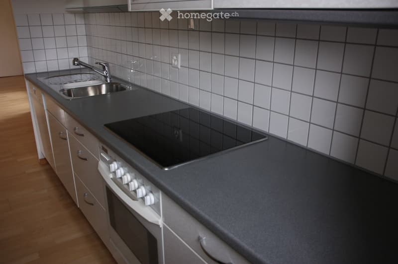 Modern kitchen with gray countertops, white tiled backsplash, stainless steel sink, induction cooktop, and built-in oven.