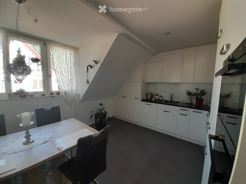 Modern kitchen with white cabinets, black countertops, a dining table with chairs, and various appliances including a sink, fridge, and oven. There are plants and decorative items on the windowsill and countertop.
