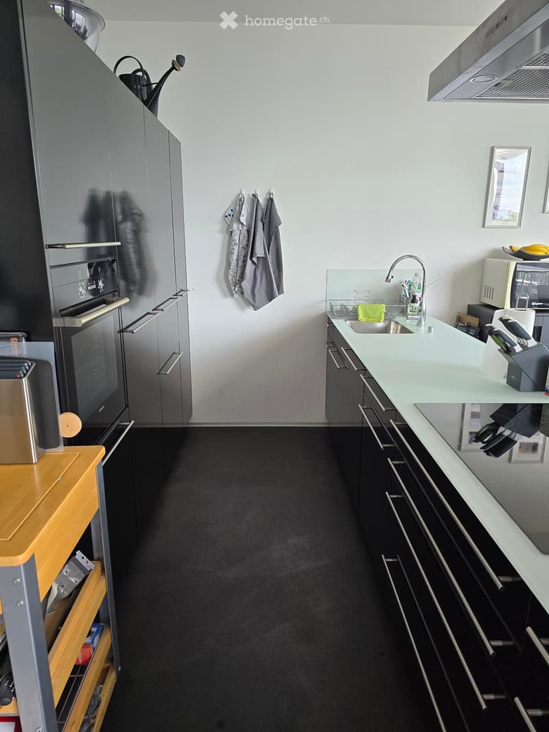 Modern kitchen with stainless steel appliances, white cabinets, and a light-colored countertop. Includes a sink, faucet, microwave, and various kitchen utensils.
