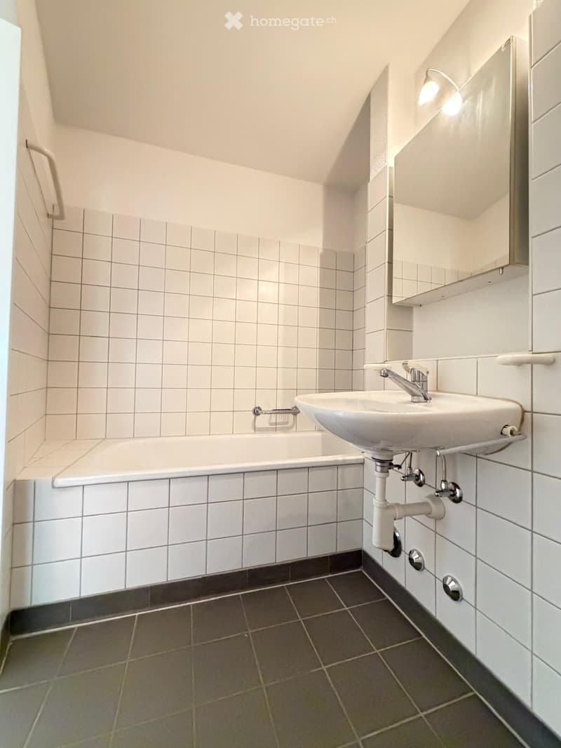 Modern bathroom with white tiled walls, a bathtub, a sink with a modern faucet, a mirror, and a built-in cabinet.
