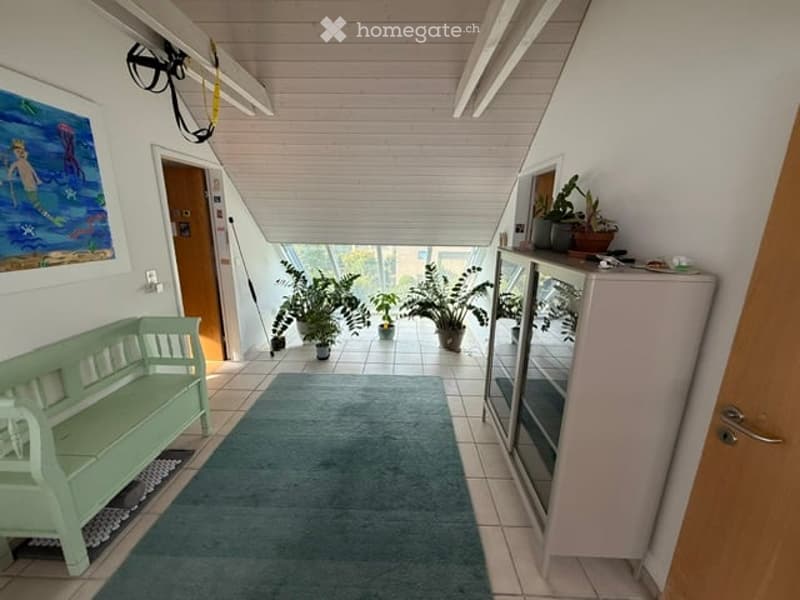 Bright hallway with wooden ceiling beams, tiled floor, green bench, potted plants, and a small cabinet with glass doors.
