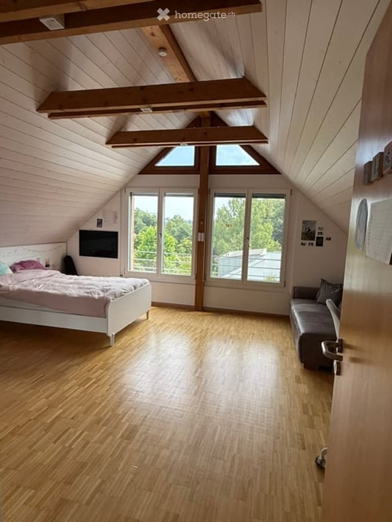 Loft-style bedroom with wooden floors, exposed wooden beams, large windows offering a view, a bed, a sofa, and a TV.
