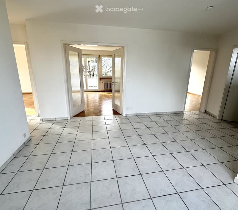 Empty room with tile flooring, white walls, white doors, open door to balcony, white radiator, no visible furniture.