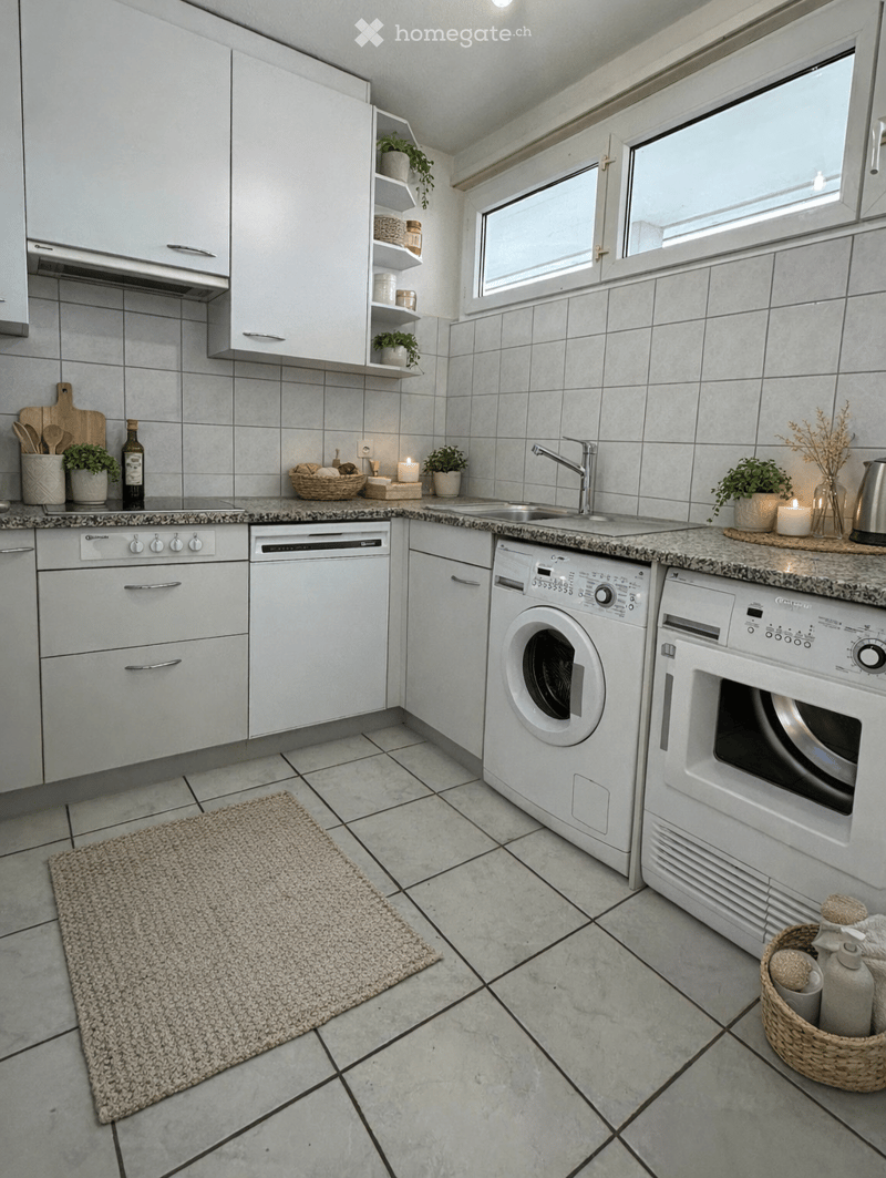 Modern kitchen with white cabinetry, tiled floor, sink, washing machine, dishwasher, white appliances, marble countertops, baskets with towels, open windows