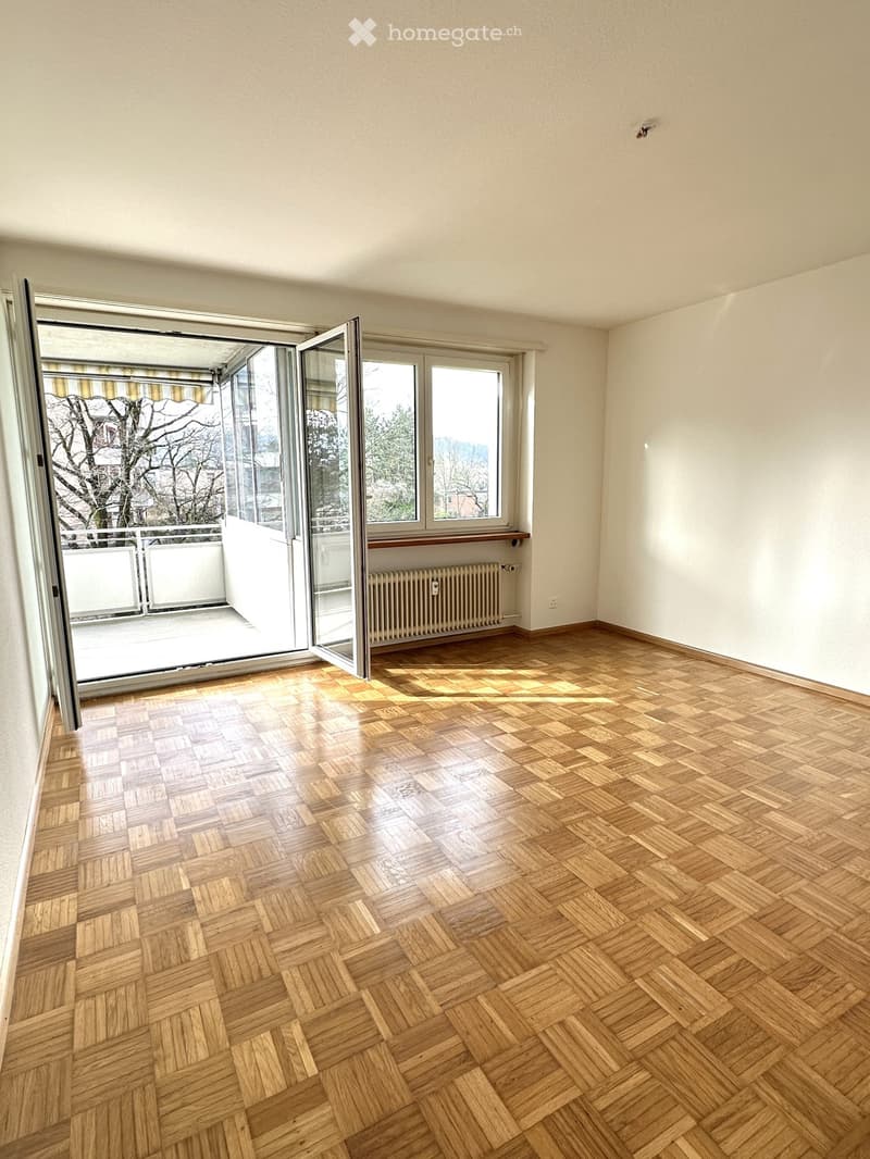 Wooden floor, white walls, open door leading to balcony, windows, balcony railing