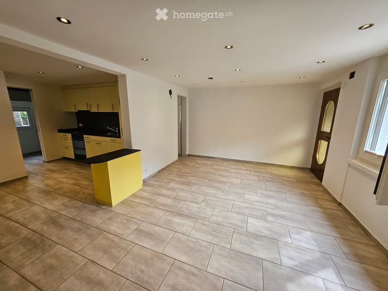 Spacious room with tiled floor, white walls, yellow kitchen island, modern kitchen setup, and a doorway leading to another room.
