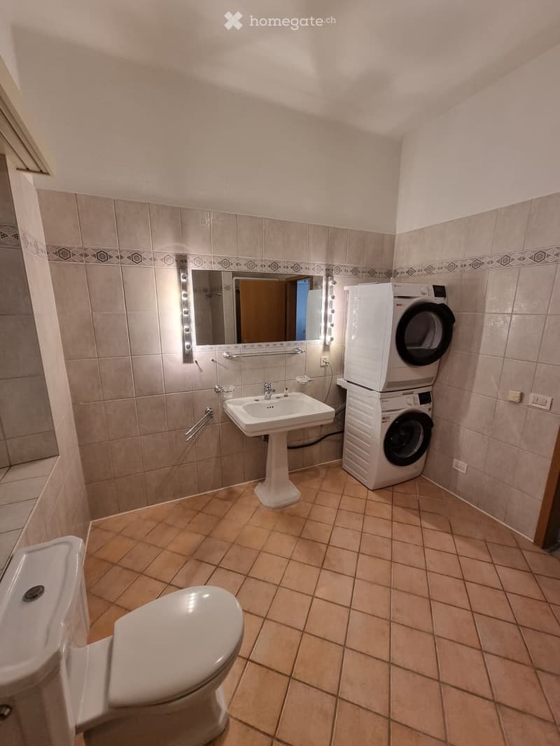 Bathroom with beige tiles, a toilet, a sink with a mirror, and a stacked washer and dryer unit.