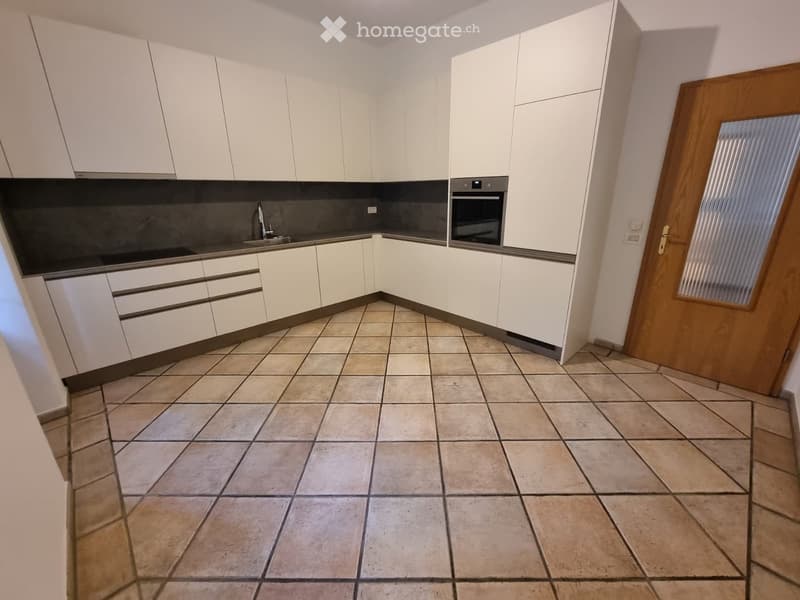Modern kitchen with white cabinets, tiled floor, and stainless steel appliances including a sink and oven.