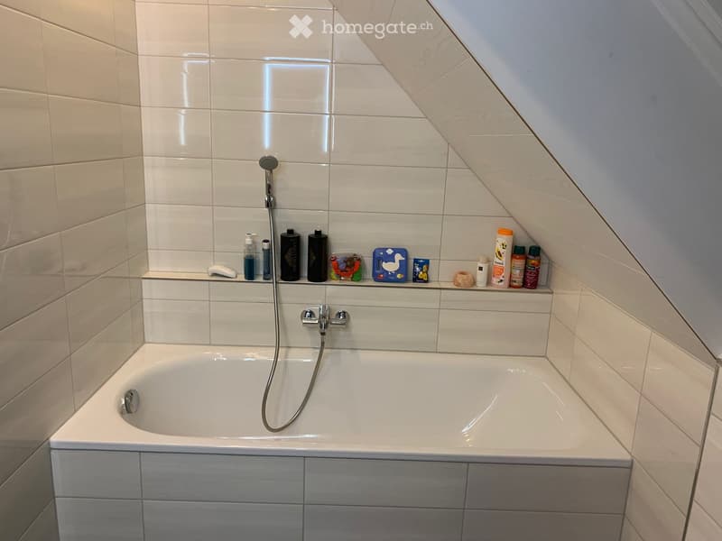 Modern bathroom with a bathtub, showerhead, and various toiletries neatly arranged on a shelf above the tub.